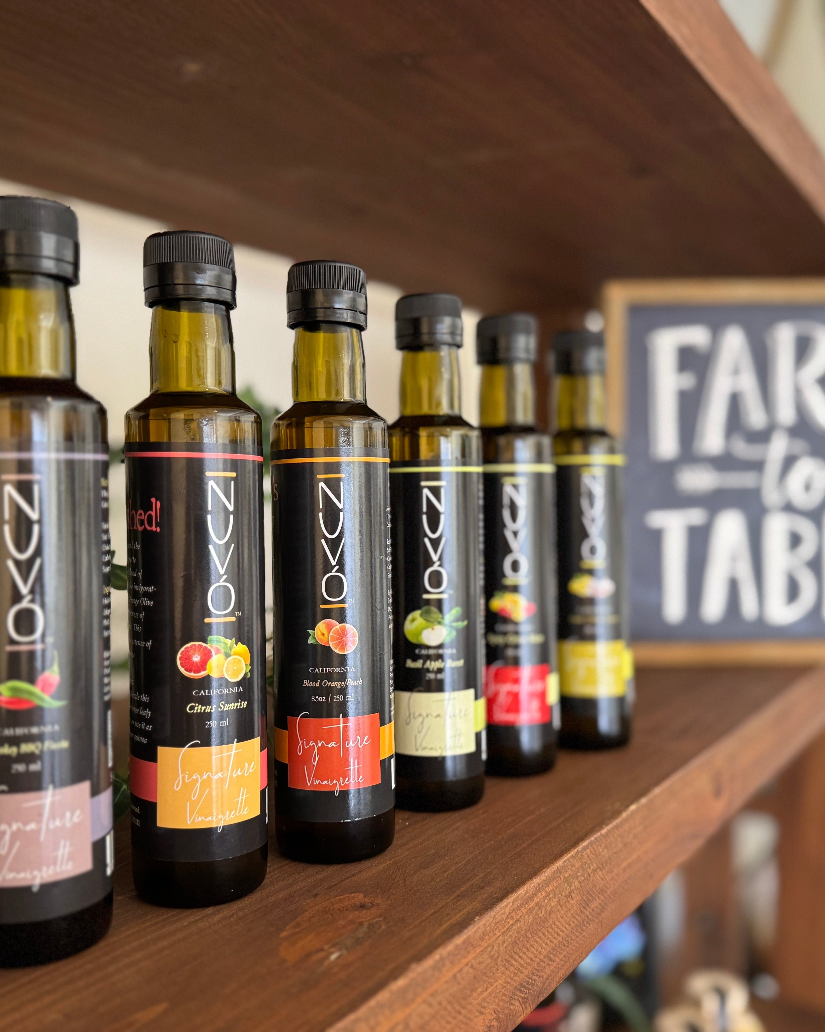 Row of olive oil bottles on a wooden shelf with 'Farm to Table' sign in the background