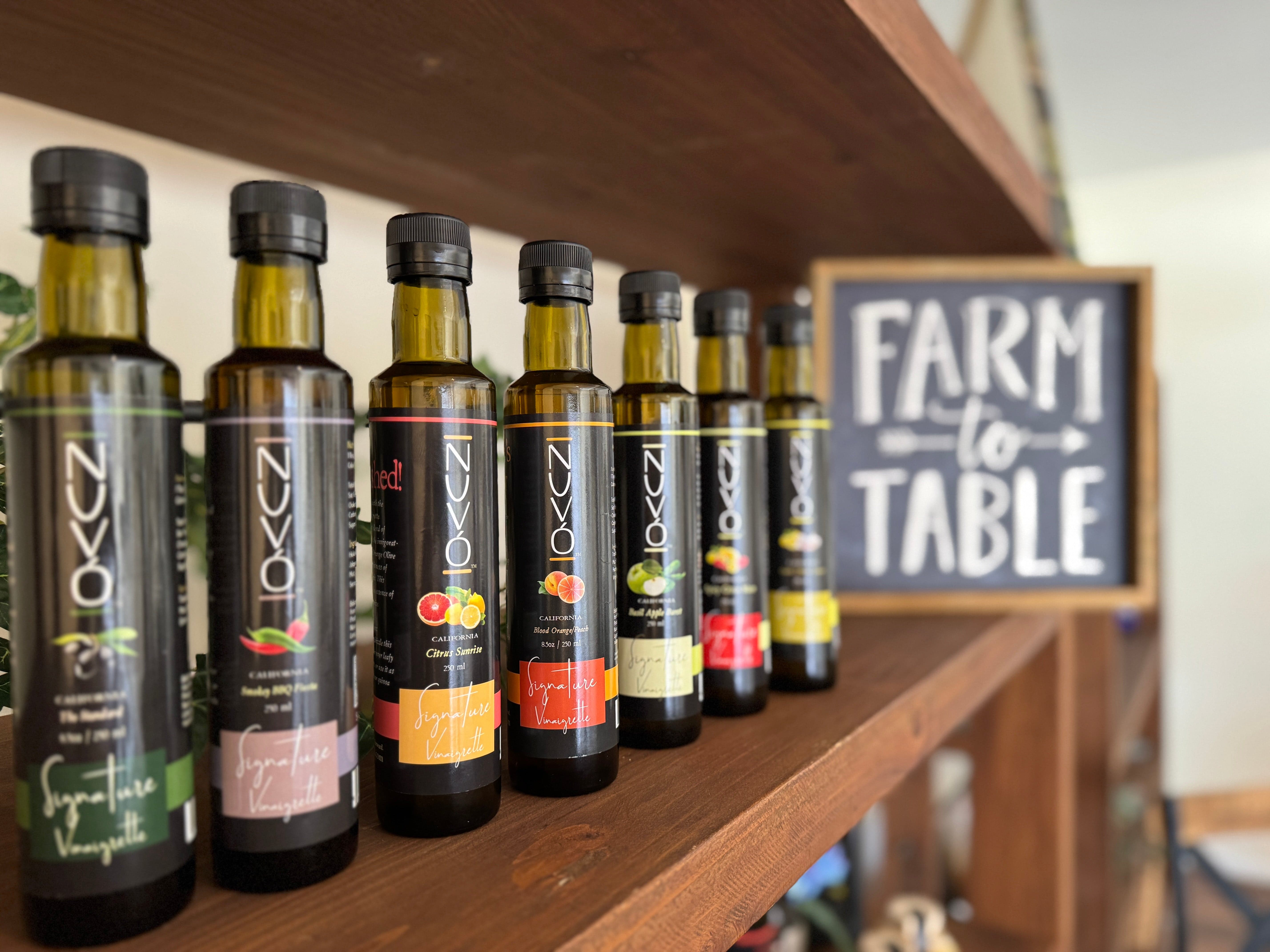 Row of olive oil bottles on a wooden shelf with 'Farm to Table' sign in the background